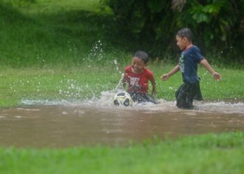 GELAGAT dua beradik, Ahmad Qhaleef Muhammad dan Ahmad Qazeem Muhaamad ceria bermain hujan di pekarangan rumah mereka yang dinaiki air di Kampung Sentul Patah, Marang, hari ini. - UTUSAN/PUQTRA HAIRRY ROSLI