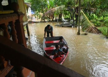 SEORANG penduduk mengawasi anaknya menaiki perahu di hadapan rumah mereka yang dinaiki air di Kampung Nibong, Kuala Berang, Hulu Terengganu. - UTUSAN/PUQTRA HAIRRY ROSLI