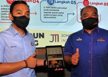 ONN Hafiz Ghazi (kanan) bersama Suhairi Hashim menunjukkan aplikasi JTI yang boleh digunakan pelancong untuk menebus baucar Pakej Pelancongan Johor di Iskandar Puteri. -UTUSAN/RAJA JAAFAR ALI
