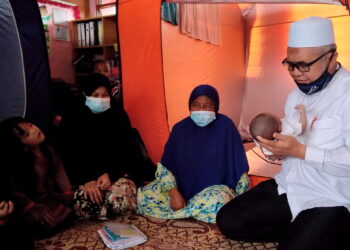 RAZMAN Zakaria mentahnik bayi lelaki berusia 22 hari di pusat pemindahan sementara Sekolah Kebangsaan Changkat Lobak di Bagan Serai, Perak, hari ini. - UTUSAN/WAT KAMAL ABAS