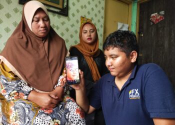 MUHAMMAD Syakawie Abdullah melihat gambar arwah bapa angkatnya, Azman Aziz sambil diperhatikan oleh Faridah (kiri) di rumahnya di Kampung Pupuh, Ampangan di sini.-UTUSAN/NOR SHAFAWATI YUP