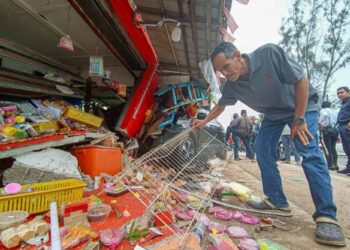 ABU BAKAR Abd. Aziz mengutip stok belacannya yang bersepah selepas gerainya di Kampung Pinang Batang Tiga, Lereh, Melaka musnah dirempuh sebuah kereta. – Utusan/SYAFEEQ AHMAD