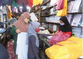 MAZIAH mengukur baju sekolah untuk anaknya, Nur Hana Atiqah Asmadi di sebuah kedai menjual peralatan sekolah di Sungai Petani hari ini. - UTUSAN/OTHMAN YAHAYA