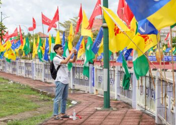 SEORANG remaja mengambil gambar  deretan bendera parti-parti politik yang akan bertanding pada PRU15 di Lubok Jong, Pasir Mas, Kelantan. -UTUSAN/KAMARUL BISMI KAMARUZAMAN