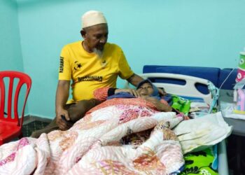 RAMLI Yahya (kiri) cekal menjaga Normah Hussin yang menghidap penyakit buah pinggang dan sakit tulang belakang di kediaman mereka di Bachang, Melaka. - UTUSAN/MUHAMMAD SHAHIZAM TAZALI