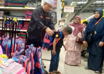 MOHAMMAD Ridzuan Suhaimi membantu Mohammad Naufal Amsyar Zakaria mencuba beg sekolah di sebuah pasar raya di Sungai Petani, Kedah, semalam. – UTUSAN/OTHMAN YAHAYA