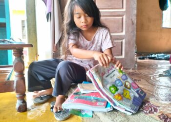 NOR Intan Ilyana menunjukkan buku teks  yang  rosak akibat rumah keluarganya di Kampung Serongga, Pasir Mas ditenggelami air baru-baru ini. –UTUSAN/ROHANA ISMAIL