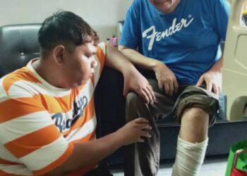 JUNAIDI Awang Kechik dibantu anak tirinya, Muhamad Fakhrul Izat Mohd. Kassim, 23, setiap kali bergerak ke mana-mana selepas kakinya dijangkiti kuman ekoran terpijak dawai kokot berkarat.