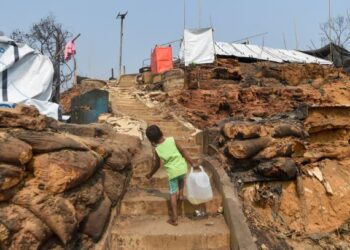 SEORANG kanak-kanak pelarian Rohingya mengangkat tong air selepas kejadian kebakaran di kem Cox's Bazar. -AFP
