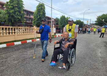 USMAN@Osman Aripin yang diiringi anaknya dibantu oleh petugas pilihanraya untuk ke pusat mengundi di Maktab Sultan Ismail, Kota Bharu, Kelantan. - UTUSAN/KAMARUL BISMI KAMARUZAMAN.