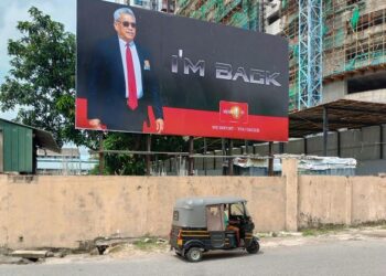 KENDERAAN roda tiga melintasi papan iklan yang menyindir kepulangan Gotabaya Rajapaksa ke Sri Lanka selepas melarikan diri ke Thailand. - AFP