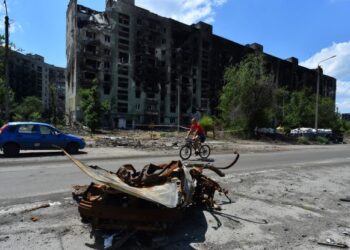 PENDUDUK menunggang basikal melepasi bangunan kediaman yang musnah di bandar Severodonetsk. - AFP