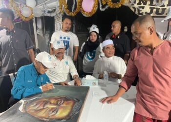 DR. Mahathir Mohamad (duduk, kiri) menandatangani potretnya yang dilukis oleh Abdul Rahman Isa, 42, yang merupakan penduduk Taman Nilam semasa Kenduri Rakyat di Langkawi, Kedah. -  UTUSAN/NUR AMALINA AZMAN