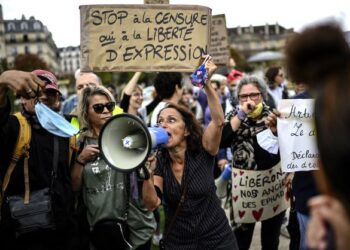 SEORANG wanita memegang sepanduk mengenai kebebasan bersuara dan menjerit menggunakan pembesar suara semasa protes menentang kewajipan pemakaian pelitup muka di Place de La Nation di Paris.-AFP