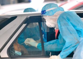 SEORANG petugas yang lengkap memakai sut PPE membantu orang ramai membuat calitan secara pandu lalu di OSCAC Stadium Tertutup Pasir Gudang di Johor. – UTUSAN/RAJA JAAFAR ALI