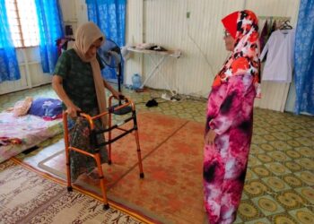ROSMIZA Awang (kiri) berjalan menggunakan tongkat sambil disaksikan kakaknya, Rubiah semasa ditemui di Kampung Kubang Bunut, Pasir Mas, Kelantan. - UTUSAN/YATIMIN ABDULLAH