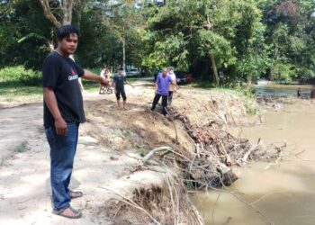 MOHD. Romzi Ahmad (kiri) menunjukkan runtuhan tebing sungai sehingga mengakibatkan jalan mini tar rosak di Kampung Paya, Baling, Kedah, baru-baru ini.