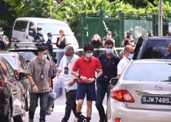 SUSPEK berbaju merah dikawal ketat anggota polis semasa dibawa ke Greenridge Crescent, Upper Bukit Timah, hari ini.-CNA/Gaya Chandramohan