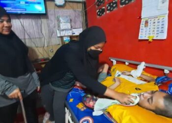 SITI Hajar Majid  (kiri) melihat Nur Amylia Shaida Mohd. Yusri membantu Irfan Fahmie yang terlantar di atas katil di Kampung Kilang Sagu, Kulim hari ini. - UTUSAN/AZAHAR HASHIM