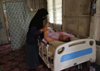 CHE Rahana Che Ngah menguruskan Mohd. Khairudin Abdullah yang terlantar selepas diserang angin ahmar dan gangguan saraf di kepala ketika ditemui di kediamannya di Kampung Pinang Merah di Paka, Dungun, semalam. UTUSAN/NIK NUR IZZATUL HAZWANI NIK ADNAN