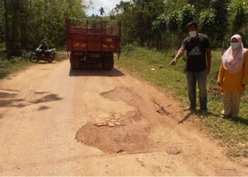 MUHAMMAD Ibrahim dan Norazura Jat menunjukkan keadaan jalan yang rosak  di Kampung Bendang Pulai, Pendang hari ini. - UTUSAN/OTHMAN YAHAYA