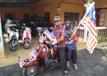 ROSMAN Marman (kiri) bersama isterinya menunggang Vespa 'Piaggio' berusia 53 tahun mengibarkan Jalur Gemilang di Felda Kota Gelanggi Dua di Jerantut, Pahang. - UTUSAN/HARIS FADILAH AHMAD
