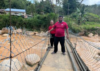 RIAN Bujang (kanan) menunjukkan jambatan gantung yang merentasi Sungai Belatop di Kampung Brooke Lama, Pos Brooke, Gua Musang, Kelantan-UTUSAN/AIMUNI TUAN LAH