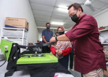 HASNI Mohammad (kanan) mencuba teknik tekanan haba dalam proses percetakan pakaian yang diusahakan Sentuhan Khalif Printing semasa mengadakan lawatan ke beberapa perusahaan usahawan kecil di Benut, Pontian, Johor.