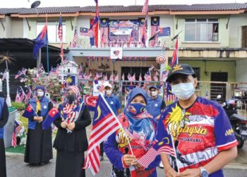 JURIAH Abdullah (dua dari kanan) dan suaminya, Zahibul Mohamad (kanan) di hadapan rumah mereka yang dihiasi 500 bendera Jalur Gemilang pelbagai saiz di Jalan Serindit 5, Taman Scientex, Pasir Gudang, Johor.