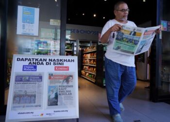 SEORANG pelanggan mendapatkan naskhah akhbar Kosmo! melalui paparan promosi Utusan Malaysia dan Kosmo! di Stesen Petronas Taman Dagang, Ampang, semalam. - UTUSAN/FAUZI BAHARUDIN