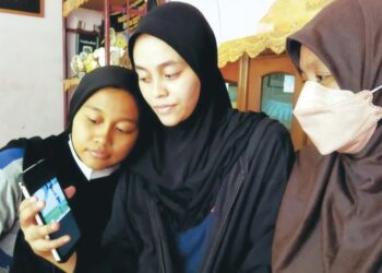 SADARIAH Mohd. Hassan (kanan) bersama dua anaknya melihat gambar Muhammad Saiful Ezzuddin Mustaffa di rumah mereka di Kampung Padang Temu, Batu 48, Baling, Kedah. - UTUSAN/NORLIA RAMLI
