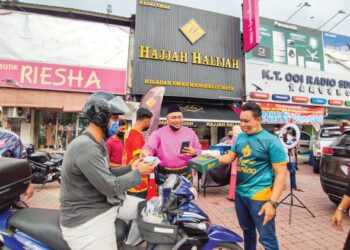 MOHD. Shaiful Hasri Shukri (kiri) bersama Faiz Johari (kanan) mengedarkan bubur lambuk dan kek Surico di hadapan Kedai Emas Hajjah Halijah, Sungai Petani, Kedah, semalam. - MINGGUAN/NUR SYAZWANA MANSOR
