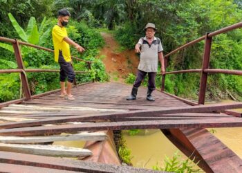 JUNOS Jusuh (kanan) dan Abdul Wahid Hasan menunjukkan sebahagian lantai jambatan besi yang rosak di Kampung Padang Toi, Sik, Kedah. - UTUSAN/NORLIA RAMLI