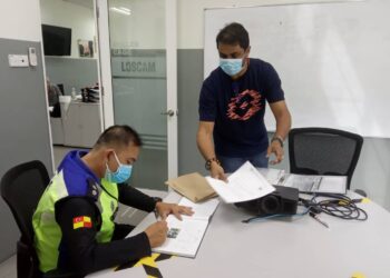 SEORANG anggota polis (duduk, kiri) memeriksa beberapa dokumen sebuah kilang di Shah Alam, Selangor, Selangor, semalam. - IHSAN POLIS 