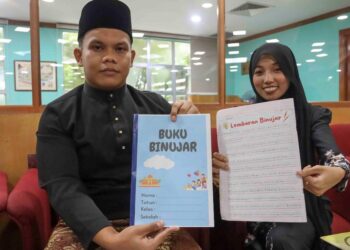 MUHAMMAD Shahrol Harun (kiri) dan Siti Farah Marzuki menunjukkan buku Bijak Menulis Abjad Berekor (Binuja) di Putrajaya. - UTUSAN/FAISOL MUSTAFA