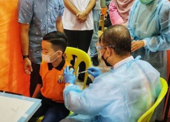 DR. NOOR Azmi Ghazali (kanan) memberikan suntikan vaksin Covid-19 kepada salah seorang murid yang hadir ke PICKids Pahang di SK Wira, Kuantan, Pahang baru-baru ini. - FOTO/DIANA SURYA ABD. WAHAB
