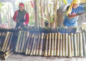 KHAZALINA Khalid (kiri) dibantu pekerjanya menyiapkan lemang untuk dijual di Kijal, Kemaman, Terengganu, hari ini. - UTUSAN/NIK NUR IZZATUL HAZWANI NIK ADNAN