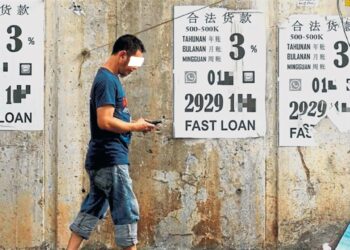 SEORANG lelaki melepasi poster-poster yang mengiklankan perkhidmatan pinjaman wang tidak berlesen. - GAMBAR HIASAN