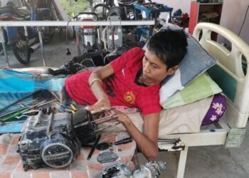MOHAMAD Zulkarnain Mustafa membaiki enjin motosikal dari atas katil kerana lumpuh di rumahnya di Chenderong Balai, dekat Pasir Salak, Perak. - UTUSAN/AIN SAFRE BIDIN