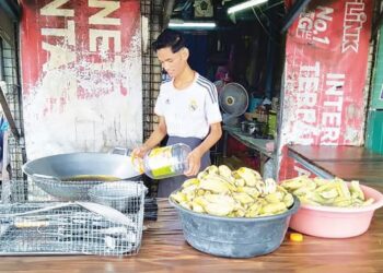 PEMBANTU gerai goreng pisang, Mohamad Hakimi Afka menuang minyak masak botol menggantikan minyak masak paket yang sukar diperolehi di Taman Ria Jaya, Sungai Petani. -UTUSAN/OTHMAN YAHAYA