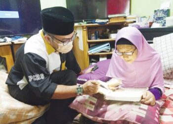 PADILAH Mustafa yang mempunyai masalah penglihatan kabur membaca al-Quran dengan bantuan cahaya telefon bimbit sambil diperhatikan Zulkifli di rumahnya di Flat Taman Sri Mawar, Senawang, Seremban. - MINGGUAN/NOR SHAFAWATI YUP