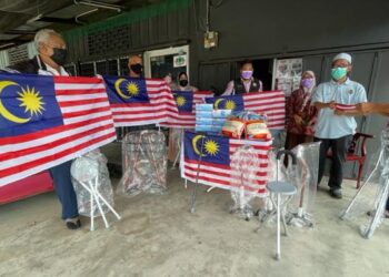 MOHD. Ramli Ab. Rahman (dua kanan) menyampaikan Jalur Gemilang dan alat keperluan sokonga asas kepada rakan OKU di Pasir Puteh, Kelantan semalam. - UTUSAN/TOREK SULONG