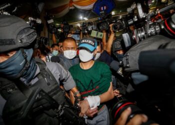 JOE FERRARI dikawal ketat pasukan keselamatan selepas meninggalkan Bahagian Pencegahan Jenayah di Bangkok.-AFP