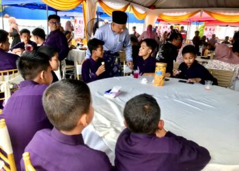 CHE Ibrahim Che Ismail (berdiri) melayan tetamu menjamu selera dalam sambutan Aidilfitri di Panji, Kota Bharu, Kelantan.- UTUSAN/ ROSLIZA MOHAMED