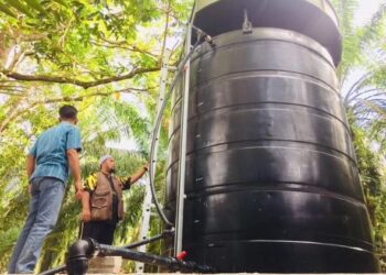 MOHD. Zakhwan Ahmad Badarddin (berdiri, kanan) melihat kerja penyelenggaraan tangki simpanan air daripada telaga tiub di Felda Sungai Retang di Jerantut, Pahang.