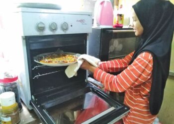 NORAIDA Zulkifli mengeluarkan sekeping piza menggunakan peralatan pemanas bersaiz kecil di Kampung Tanjung Buloh di Lipis, Pahang. - UTUSAN/HARIS FADILAH AHMAD