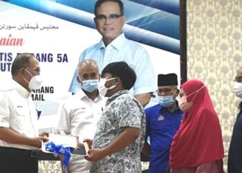 WAN ROSDY Wan Ismail (kiri) menyampaikan replika kunci dan surat hak milik Rumah Rakyat Pahang kepada penerima, Muhammad Muzakir Ben Yazeed (tengah) di Jerantut, Pahang. - FOTO/HARIS FADILAH AHMAD