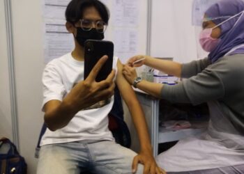 LUQMAN Hakim Suhaimi merakam video semasa dia menerima vaksin di PPV IPT Mega UiTM Shah Alam, Shah Alam, Selangor pada 29 Julai 2021. - UTUSAN / MOHAMAD NAUFAL MOHAMAD IDRIS