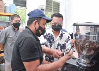 TUANKU Syed Faizuddin Putra Jamalullail bercemar duli mencuba membuat kopi sempena pembukaan cawangan ke-88 Richiamo Coffee sambil diperhatikan Wan Najib Wan Daud (kiri).