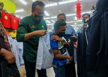 MOHD. Salim Mohd. Sharif (kiri) menyarungkan pakaian sekolah kepada seorang pelajar pada Program Happy To School Parlimen Jempol Bersama Risda di sebuah gedung pakaian di Bahau Jempol hari ini.- UTUSAN/NURULAZMA SHAFIQAH KHAIRUL AZHAR.